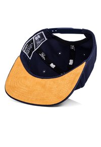 Navy cotton cap with a tan suede brim, featuring an adjustable strap and internal labels, highlighting its construction and design details.