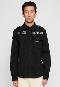 Fekete, pamutból készült gombos ing katonai stílusú részletekkel, két elülső zsebbel és "Iron Maiden" hímzéssel a mellkasán.