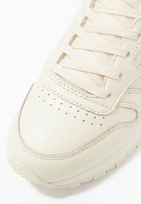 Baskets en cuir crème avec une texture lisse, des détails perforés sur l'avant-pied et des lacets plats. Dotées d'une semelle coussinée.