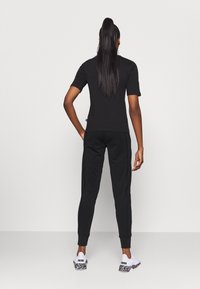 Schwarzes Kurzarmshirt und passende Jogginghosen aus glattem Stoff. Die Jogginghosen haben Seitenstreifen und Bündchen an den Knöcheln. Sneaker mit einem gemusterten Sohlenprofil.