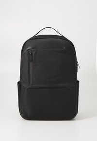 Sac à dos noir avec une finition lisse et mate, doté d'une poche zippée à l'avant et d'une poche en mesh sur le côté. Poignée supérieure robuste pour deux options de port.