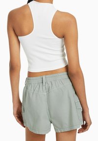 Bílý žebrovaný crop top s vysokým výstřihem v kombinaci se zelenými šortkami s elastickým pasem a bočními kapsami.