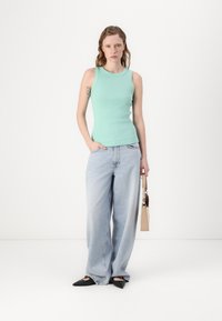 Mintgrønn ribbet tanktop kombinert med lyseblå vide jeans og svarte spisse leiligheter; holder en beige håndveske. Enkelt og uformelt antrekk.