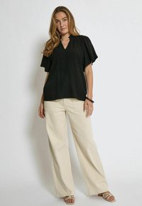 Top nero a maniche corte con scollatura a V e dettagli arricciati, abbinato a pantaloni beige a gamba larga. Tessuto liscio e vestibilità rilassata.