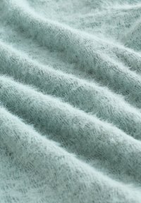 Weicher, hellblauer Stoff mit einer flauschigen Textur, der ungleichmäßige Falten aufweist und eine leicht transparente Qualität besitzt, die seine zarte Beschaffenheit betont.