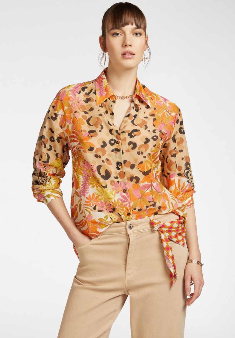 Camicia a maniche lunghe con stampa floreale e maculata in toni di arancione, rosa e beige. Tessuto leggero con una vestibilità rilassata, abbinata a pantaloni beige.