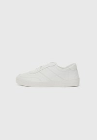 White leather sneaker with flat laces, rounded toe, and subtle stitching details. Features a textured sole and embossed brand logo on heel.