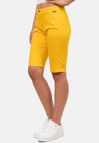 Geel denimshorts met een slim fit, voorzien van broekzakken aan de voorkant, een knoopsluiting en een nette zoom. Gepaard met witte sneakers.