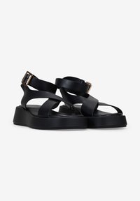 Black sandals featuring wide cross straps, a chunky platform, and a side buckle detail. Made of smooth synthetic material.