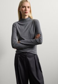 Haut gris à manches longues avec un col haut, associé à un pantalon plissé foncé. Texture douce, design ajusté et style minimaliste.