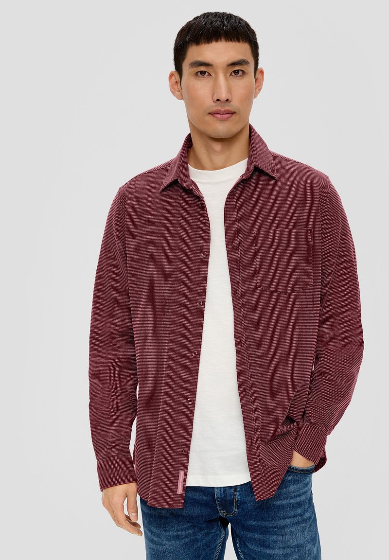 Burgundowa koszula w kratę z długim rękawem, z kieszonką z przodu i miękką teksturą, nałożona na białą koszulkę i zestawiona z niebieskimi dżinsami.