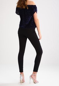 Granatowa bluzka z odkrytymi ramionami o welurowej fakturze, połączona z czarnymi rurkami z przetarciami i srebrnymi sandałami na obcasie.