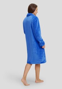 Bata de felpa azul con cuello de chal y mangas largas, con una textura suave y un diseño hasta la rodilla. Sin cierres visibles.