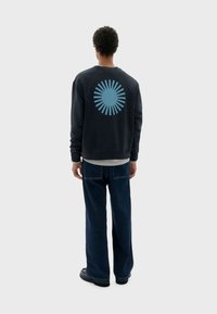 Sudadera azul marino con un diseño de estallido de sol en azul claro en la parte posterior, combinada con jeans azul oscuro y zapatos negros.