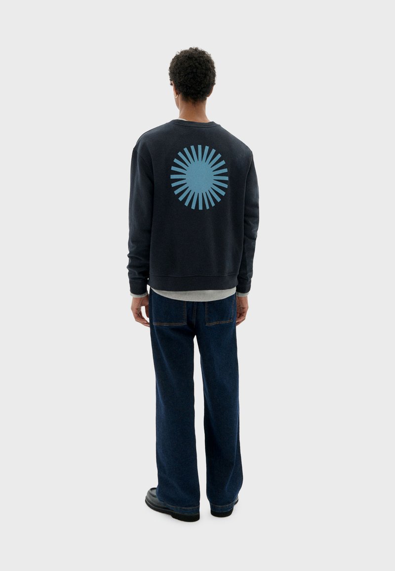 Sudadera azul marino con un diseño de estallido de sol en azul claro en la parte posterior, combinada con jeans azul oscuro y zapatos negros.