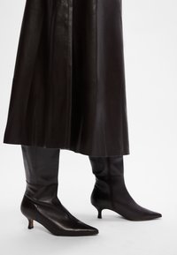Svarta läderstövlar till mitten av vaden med spetsiga tår och en liten klack, med en glatt textur och minimalistisk design.