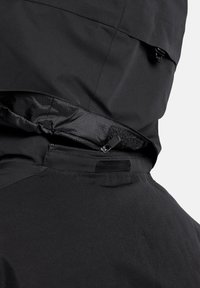 Schwarze wasserdichte Jacke im Detail, mit einer Reißverschlusstasche und einem Klettverschlussdeckel, glatter Textur und matter Oberfläche.