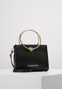 Svart läderhandväska med guldaccessoarer, utrustad med ett cirkulärt handtag och hjärtdetalj. Logotypen "VALENTINO" i guld framtill.