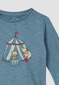 Blaues Kinderlangarmshirt mit einem Zelt des Zirkus, einem Löwen auf einem Sockel und einem Elefanten, der auf einem roten Ball balanciert, auf der Vorderseite.