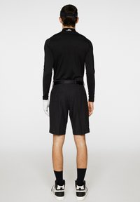 Czarna koszula z długim rękawem, czarne szorty i białe rękawiczki. Widok z tyłu, ukazujący prosty design, jednolity kolor i sportowy krój. Czarne trampki z akcentami.