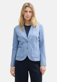 Blazer bleu clair avec deux poches avant, fermeture à un bouton et un tissu lisse. Manches longues et coupe ajustée.
