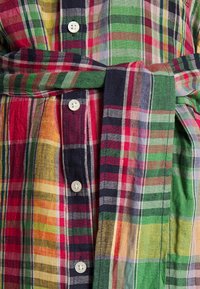 Mehrfarbiges Karomuster-Hemd mit grünen, roten, gelben und blauen Streifen, mit weißen Knöpfen vorne geknöpft und einem gebundenen Taillengürtel.
