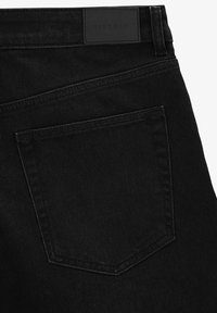 Jeans in denim nero con tasca a toppa e etichetta rettangolare in vita. Il tessuto ha una texture liscia con dettagli di cucitura sottili.