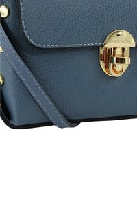 Blauwe leren handtas met een gestructureerd oppervlak, voorzien van een gouden slotsluiting, decoratieve gouden studs en contrasterende donkere randen. Inclusief schouderriem.