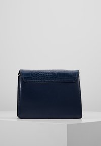 Marineblå håndtaske med en tekstureret krokodillemønster på klappen, slankt design og glat læderfinish.