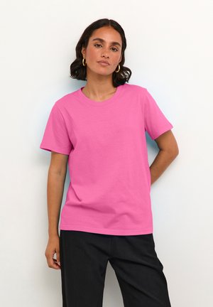 Pink bomulds T-shirt med rund halsudskæring og korte ærmer. Sammen med sorte bukser, præsenteret mod en ensfarvet lys baggrund.