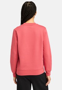 Sudadera rosa de manga larga, con cuello redondo, puños y dobladillo acanalados. Textura suave y ajuste casual, combinada con pantalones negros.