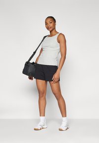 Top gri fără mâneci și pantaloni șort negri, poză în picioare. Pantofi sport albi, geantă neagră cu curea de umăr, material neted și croială ajustată.