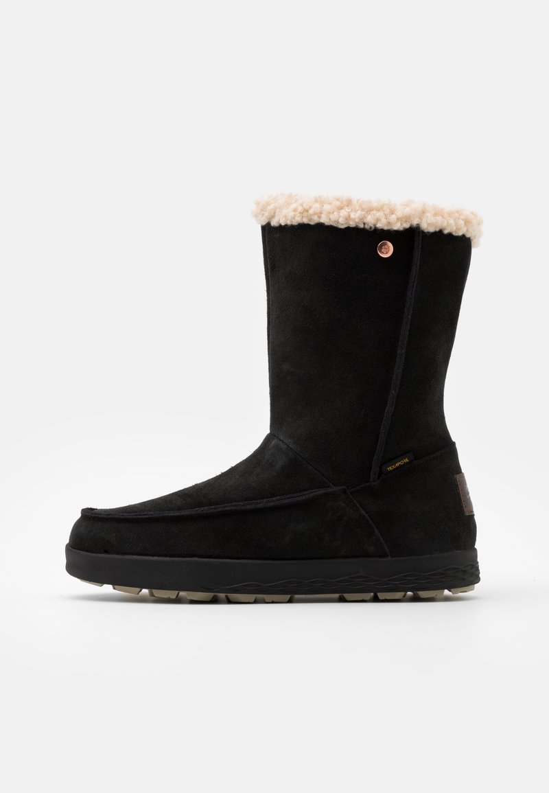 Botte d'hiver en suede noir avec doublure en fourrure crème, bout arrondi, détails cousus, semelle en caoutchouc et un petit logo en métal sur le côté.