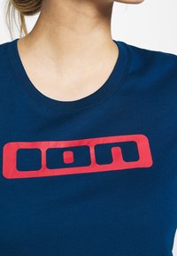 Navy blue cotton t-shirt featuring a large red graphic logo with rectangular shapes and a central circle. Round neckline displayed.