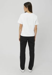T-shirt en coton blanc à manches courtes, associé à un jean en denim noir. La tenue est complétée par des baskets blanches et des bijoux minimalistes.