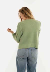  Lichtgroene gebreide trui met een gestructureerd ribontwerp, cropped lengte en lange mouwen, gecombineerd met hoge taille blauwe denim jeans.