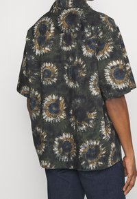 Camicia a maniche corte in tessuto verde scuro con un motivo di girasoli impreziosito da accenti gialli, bianchi e blu. Vestibilità rilassata.