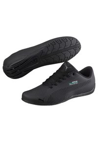 Svarta sportskor i syntetmaterial, med ett perforerat mönster, texturerad sula och detaljerad logotyp på sidan.