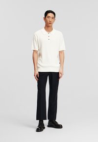 Witte textuur polo shirt met een kraag en drie knopen, gecombineerd met zwarte op maat gemaakte broeken. Zwarte veterschoenen maken de look compleet.
