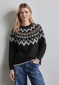 Svart tröja med geometriskt mönster i grått och beige. Ribbad halsringning och manschetter, kombinerad med blå jeans. Slät textur, avslappnad passform.