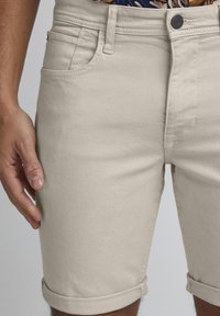 Pantaloncini in denim beige con classico design a cinque tasche, orli risvoltati e chiusura frontale con bottone nero a contrasto.