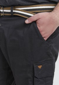 Sorte cargo bukser med sidelommer og et vævet bælte i guld, hvidt og sort stribede. Glat tekstur og afslappet design.