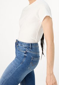 Camiseta de algodón blanca combinada con jeans de mezclilla azul de tiro alto, que presentan una silueta ajustada y un diseño minimalista.