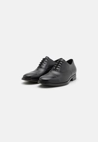 Zapatos de vestir de cuero negro con punta redondeada, diseño de cordones y un sutil detalle en la puntera. Tacón bajo y textura suave.
