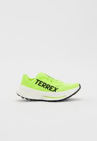 Neon zöld sportcipő hálós felsőrésszel, vastag fehér középtalppal, fekete "TERREX" márkázással, és texturált fekete talppal a tapadás érdekében.