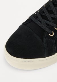 Sneaker in suede nera con punta rotonda, parte superiore testurizzata e lacci neri. Presenta occhielli in metallo e una suola in gomma di colore crema.