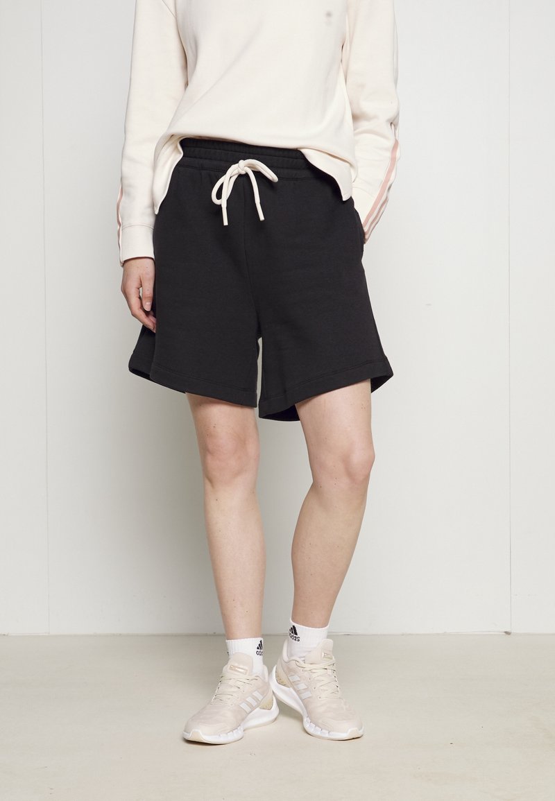 Svarta bomullsshorts med elastisk midja och dragsko, med sidofickor. Stylen är kombinerad med en ljusfärgad långärmad topp.