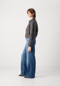 Giacca in tweed bianco e nero con design corto, abbinata a jeans blu a gamba larga. L'insieme presenta un colletto classico e trame contrastanti.