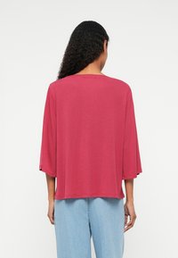 Magenta oversized top with three-quarter sleeves, soft texture, round neckline, and a relaxed fit, paired with light blue wide-leg jeans.