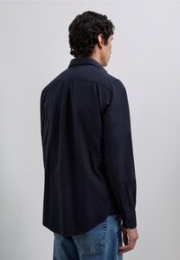 Camisa azul marino de botones con cuello, mangas largas, yugo trasero, y un dobladillo ligeramente curvado. Tejido ligero con una textura suave.